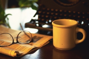 Typewriter, newspaper, glasses and a cup of coffee on desk, high angle view, close up